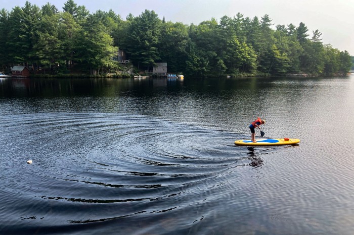 A boy gunwale bobbing on a paddleboard creating large ripples on the surface of a lake