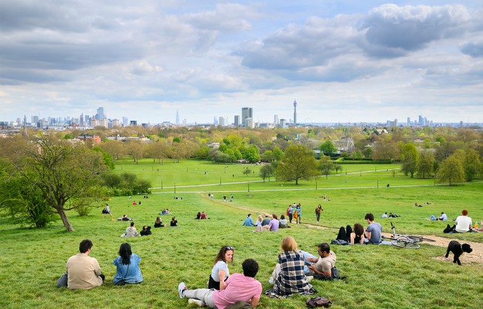 View from Primrose Hill, North London. Young people relaxing on the grassy slopes of Primrose Hill park with uninterrupted views of buildings on the London skyline.