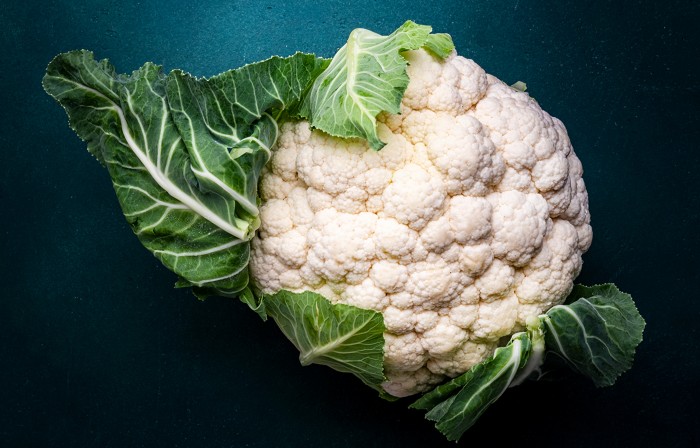 Fresh organic white cauliflower cabbage with leaves on old rustic green table background, top view.