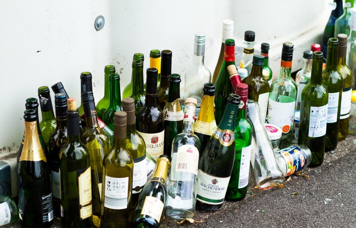 Line up of many empty sparkling wine and champagne bottles left on the ground on the side of a street in Germany.