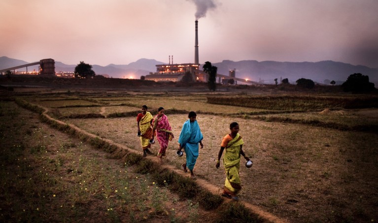 Women walk through a field in front of the Vedanta Alumina plant in Lanjigarh.