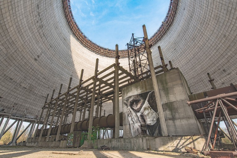 A mural close-up of a person's face, wearing a surgical mask, in a circular derelict structure full of scaffolding.