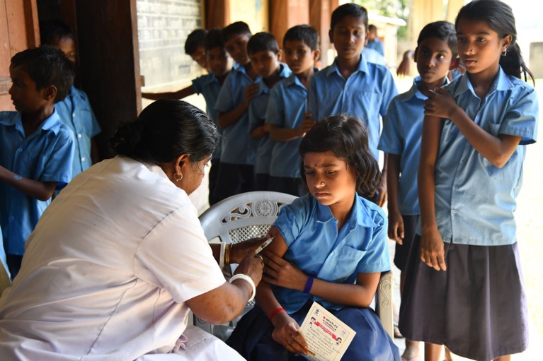 An India health worker injects a school pupil with a measles and rubella vaccine while other pupils wait to receive the vaccine