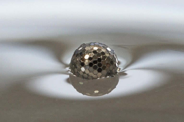 A liquid droplet coated with shiny solid particles floating on the surface of water