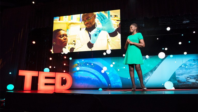 Faith Osier smiles while standing in front of LED screens during her TED presentation in Canada, 2018