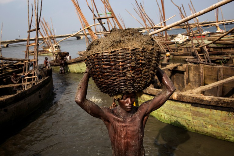 A labourer carries away large basket of wet sand that has been dug from the seafloor of the Lagos Lagoon.