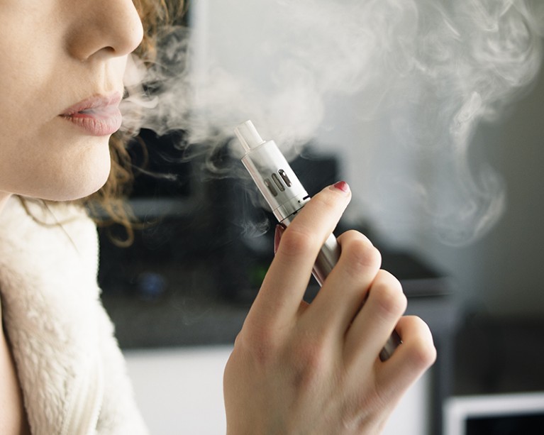 Close-up of a young woman exhaling smoke vapour from an e-cigarette
