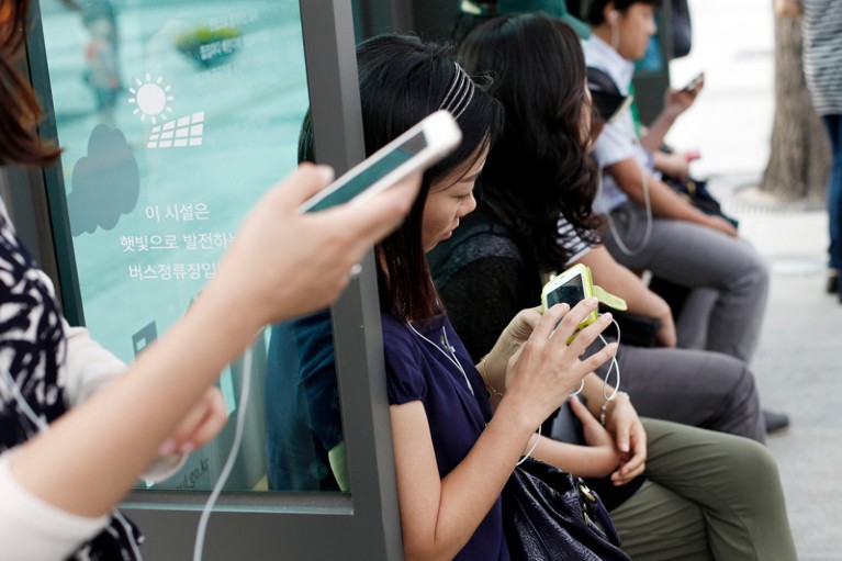 Passengers waiting at a bus station using smart phones