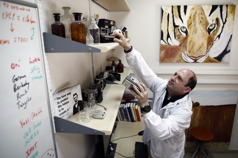 Noam Shomron in his lab office, with his paintings and camera collection near his desk