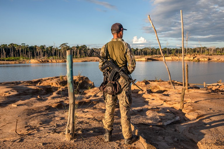 An armed Peruvian soldier looks over the remains of the La Pampa illegal gold mine