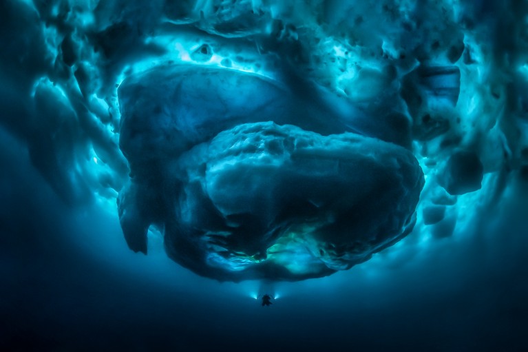Underwater view of a diver shining lights on the bottom of a large glacier