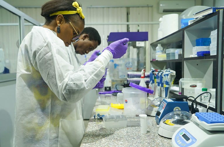 Two students in lab coats work at a lab bench