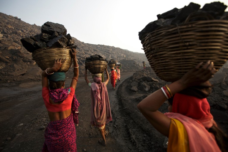 Women in brightly coloured traditional Indian dress carry large baskets full of coal on their heads