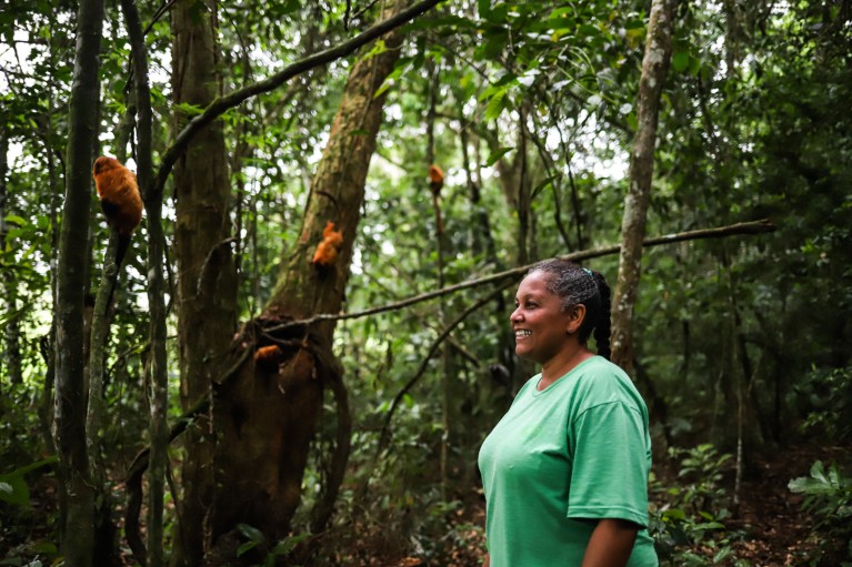 Andreia Martins stands among some trees in which sit a few golden lion tamarins