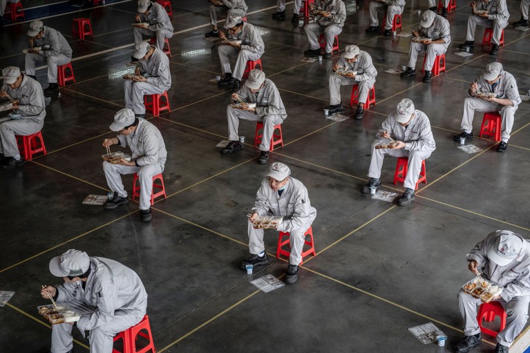 Factory workers in China eat their lunch under social distancing restrictions sitting on spaced out red stools