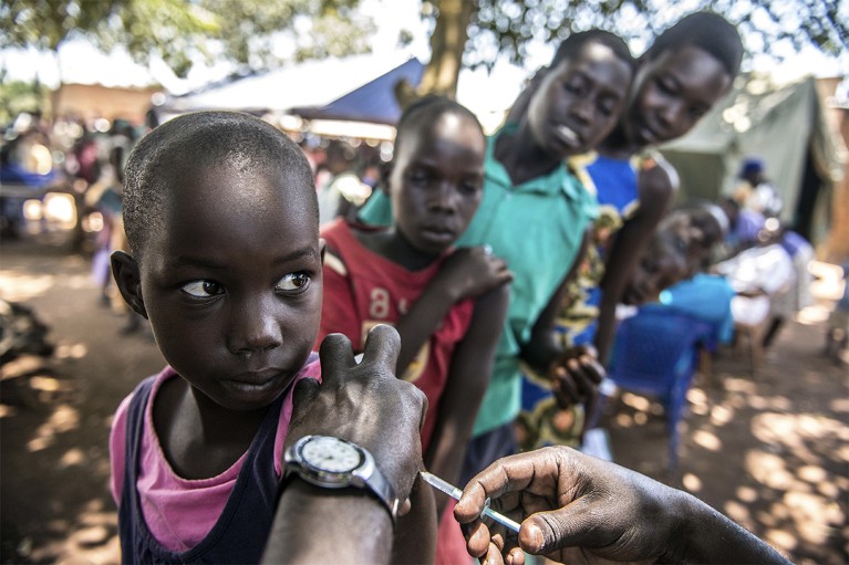 A young girl at the front of a queue receives an injection in her upper arm