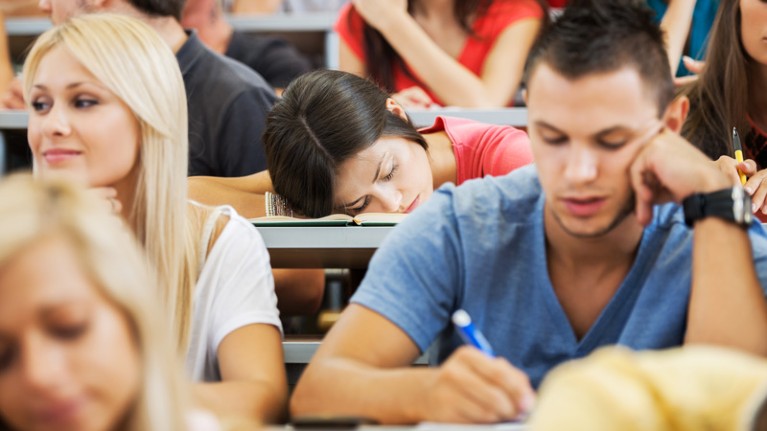 Young woman and young man in a lecture with a female student sleeping in the row behind them.