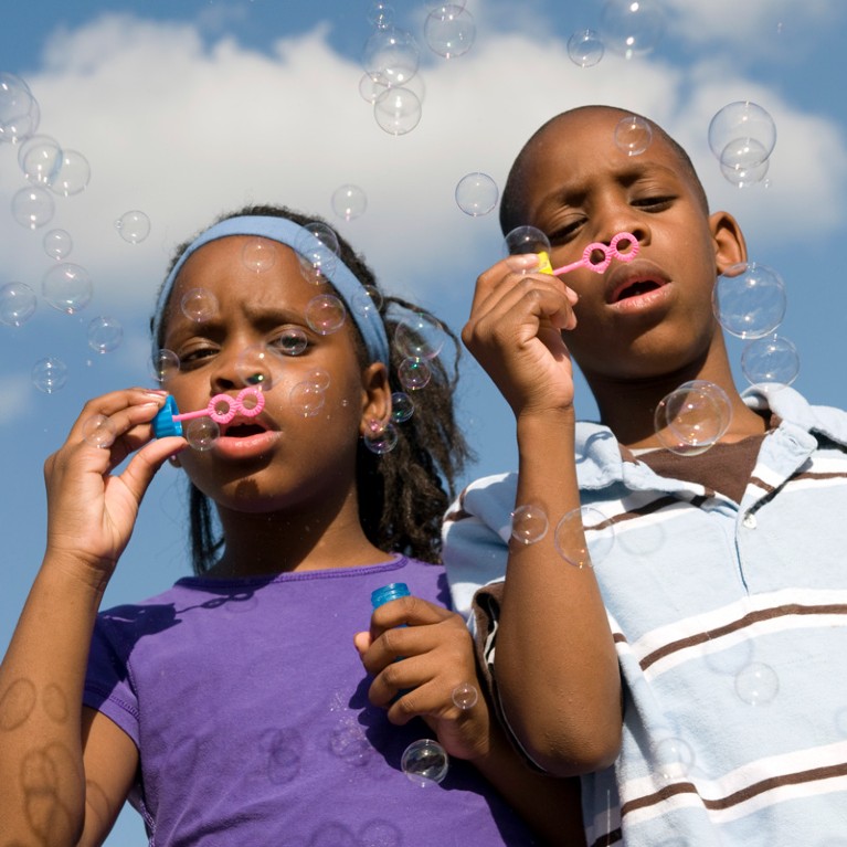 Twin brother and sister blowing bubbles outside on a sunny day.