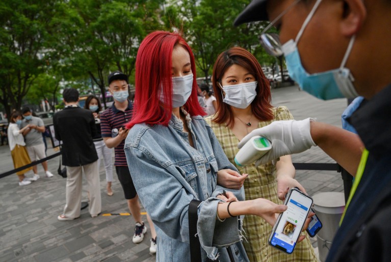Women in Beijing display a health QR code on their phones as a security guard takes their temperature with a remote sensor