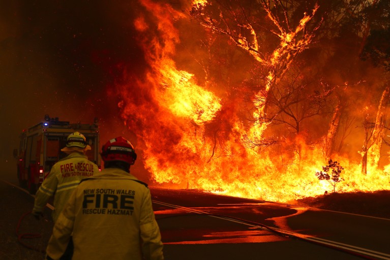 Fire and Rescue personnel run towards a fire truck as a bushfire burns next to a major road