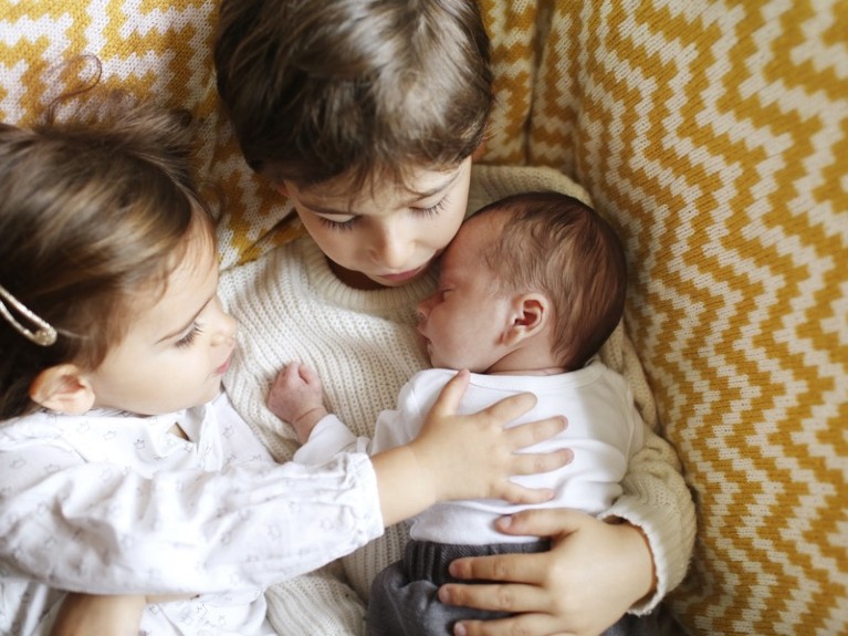 A baby in the arms of his big brother and sister.