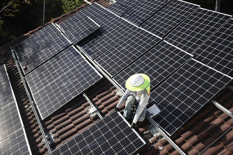 Person in wide-brimmed hat installing solar panels on the roof of a house.