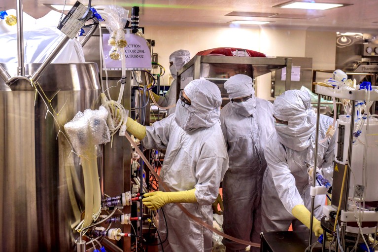 Three workers in protective clothing work on a bioreactor in a vaccine producing facility in Pune, India