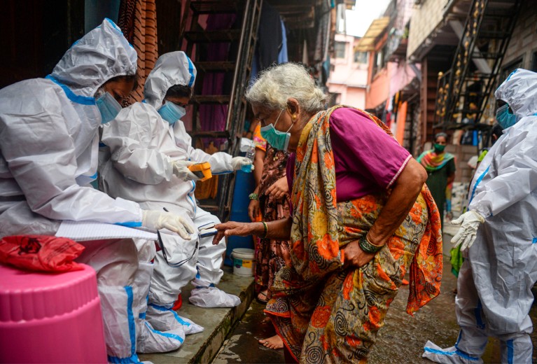 Health workers wearing coveralls and masks check the temperature of an elderly woman in the Dharavi slum in Mumbai