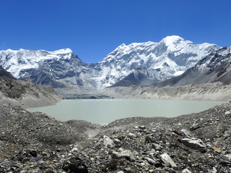 Rocky surface in foreground with grey-blue lake behind it and snow-covered mountains in the distance.