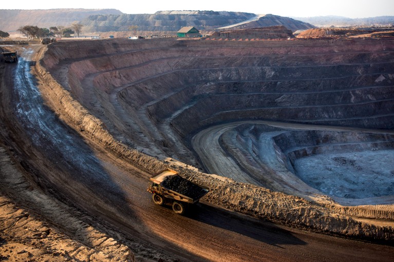 A truck drives around the edge of a open pit copper mine at sunset