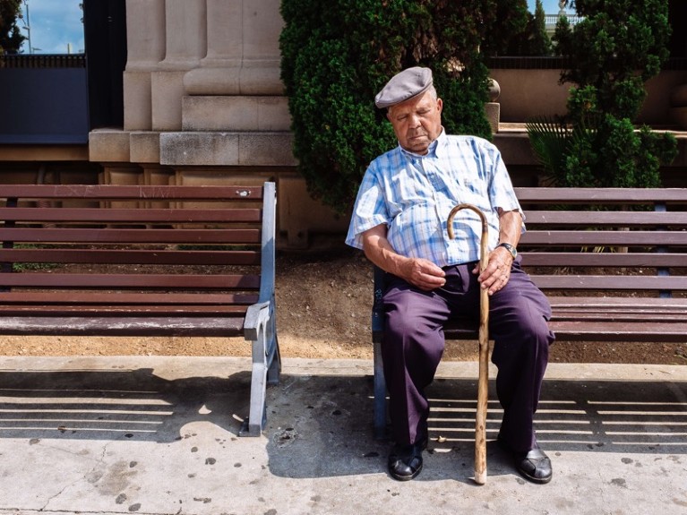 Old men wearing a typical beret sleeping while sitting on a public bench.