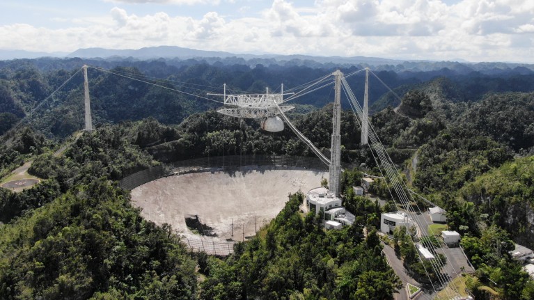 Wide aerial shot showing a hole in the main collecting dish of the Arecibo Observatory radio telescope.