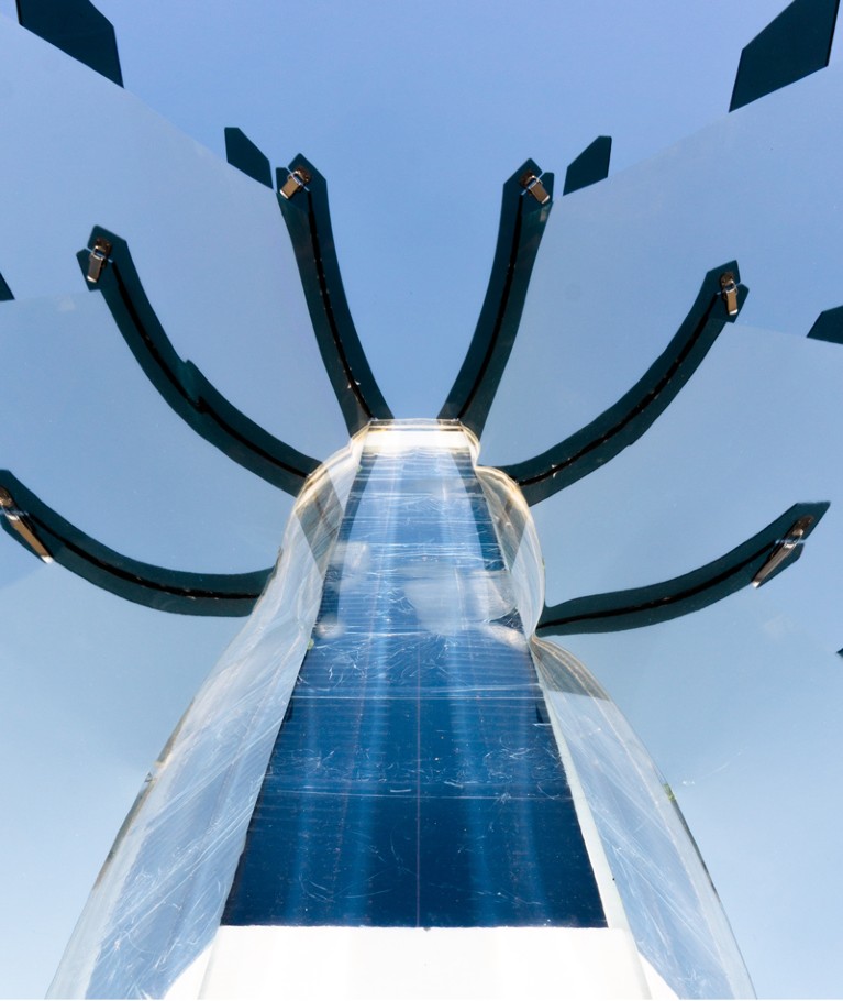 A solar collecting device with mirrors around a central core, framed against a blue sky.