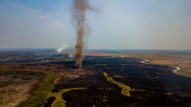 An aerial view of a plume of smoke rising from a burnt landscape