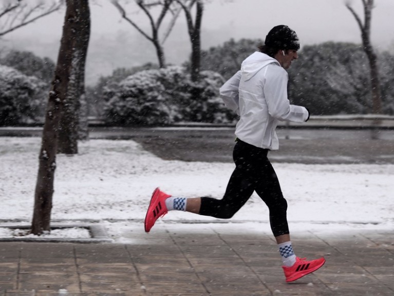 A man jogging on a snowy street.