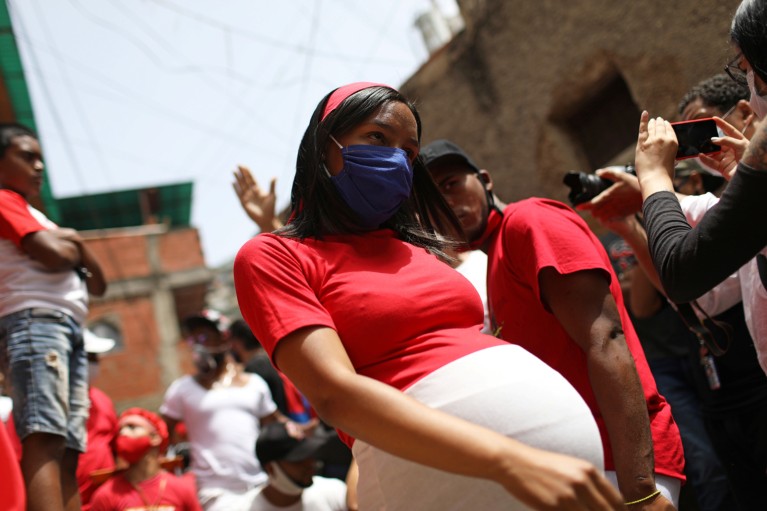 A heavily pregnant woman wearing a face masks and red t-shirt walks through a crowd amid feast day celebration in Venezuela
