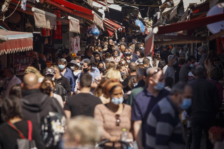 A narrow street in Tel Aviv filled with people, some wearing face coverings