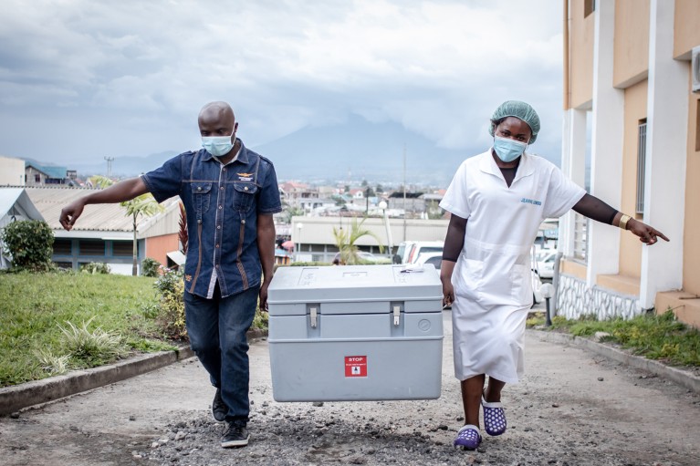 Two health workers carry a large crate containing COIVD-19 vaccines up a hill in Goma, Democratic Republic of Congo