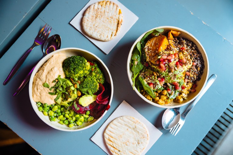 Birds-eye view of vegan bowls with various vegetables and seeds on a blue table