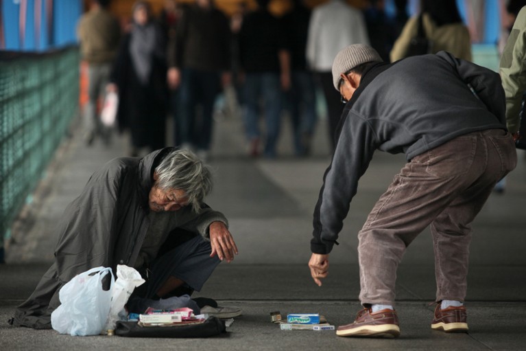 A passer-by stops to give money to a homeless man sitting on the street in Hong Kong