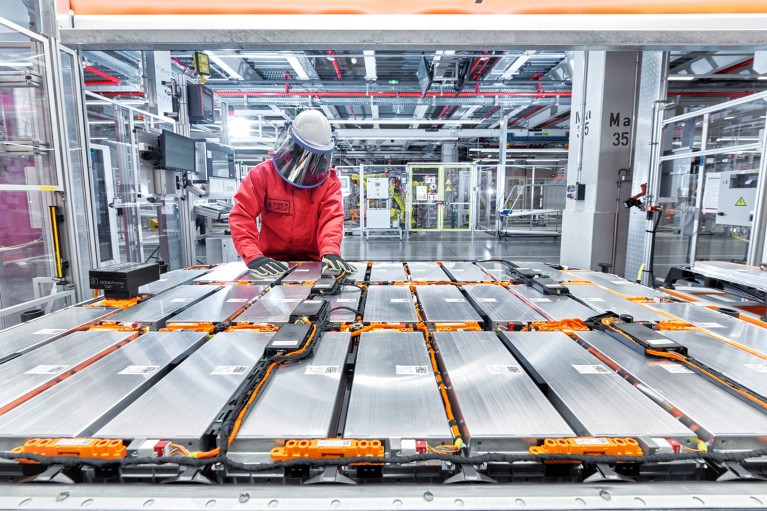 A worker wearing a face visor assembles an array of battery modules for an electric vehicle