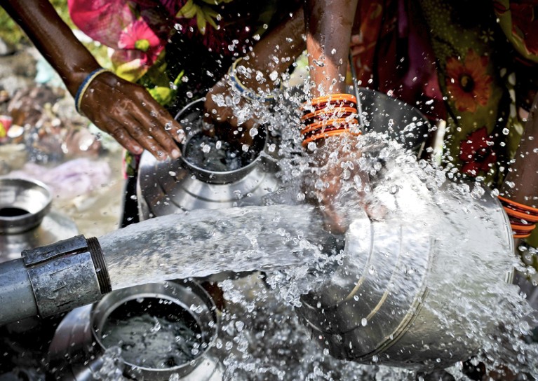 Close up of people collecting water from a ground-water pump in India