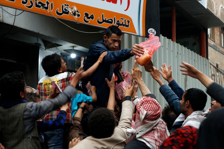 Yemenis reach to grab food being handed out at a charitable centre
