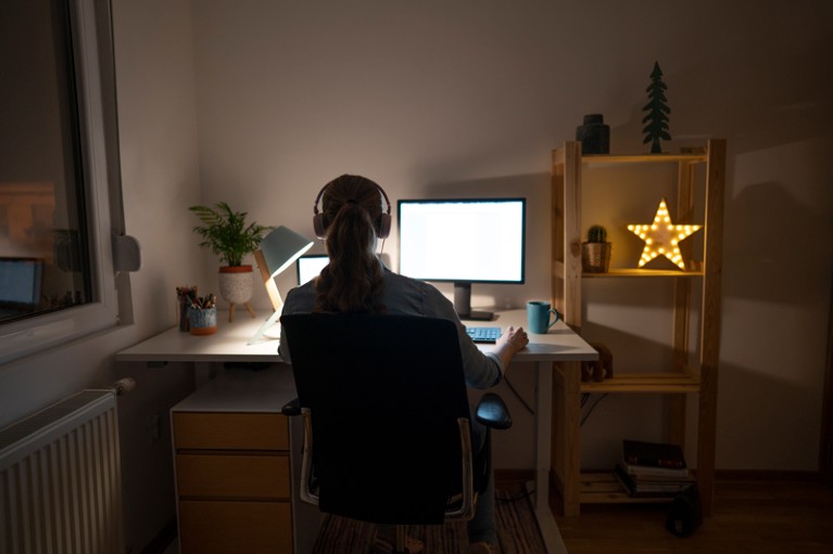 Rear view of a young woman working late on her computer in her home office