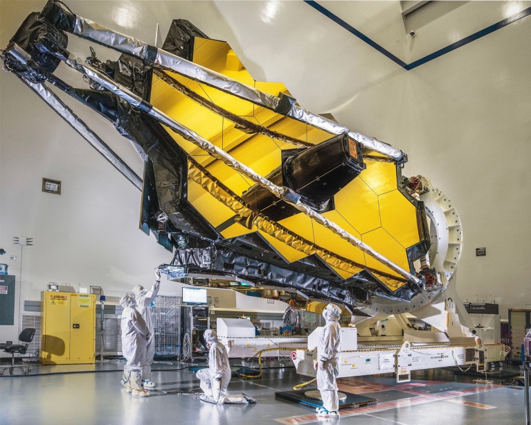 Technicians in white overalls inspect the optical portion of the James Webb Space Telescope in a clean room at Northrop Grumman
