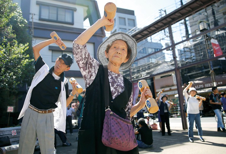 People stand in a courtyard exercising with hand-held dumb-bells