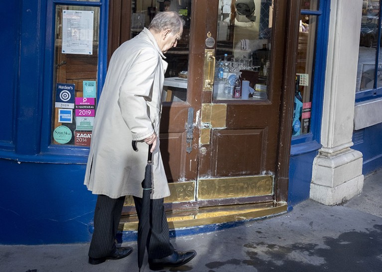An elderly gentleman carrying an umbrella walks past the doorway of a restaurant in London, England.