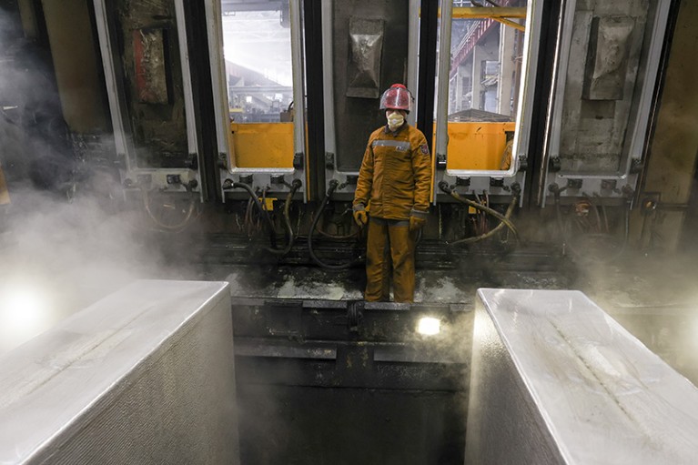 A worker in protective gear removes bars of aluminium from a casting machine at Rusal's Bratsk Aluminium Smelter.