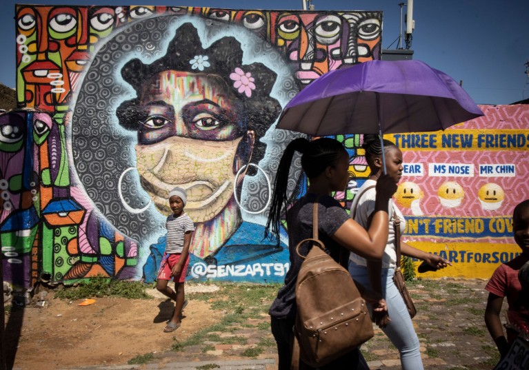 Soweto residents walk past a mural educating people about the dangers of the coronavirus and mask wearing