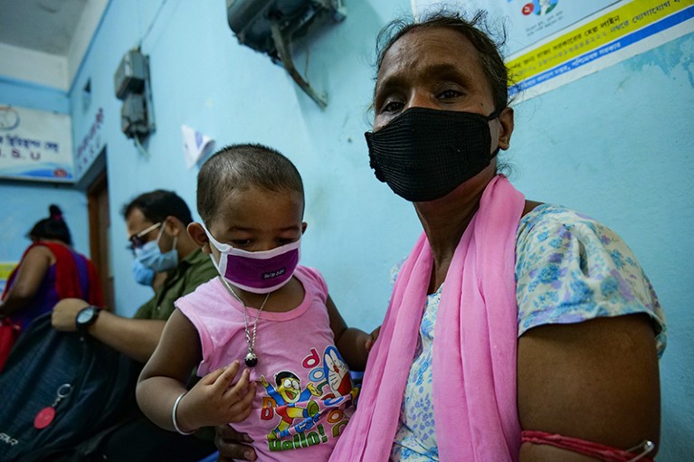 A child and his mother, both wearing safety face masks, waiting at a vaccination center in Kolkata, India.